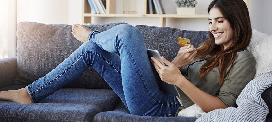 women smiling laying on a couch looking at her tablet holding her card