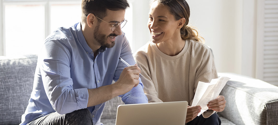 young man and woman sitting on a couch with paper and a laptop