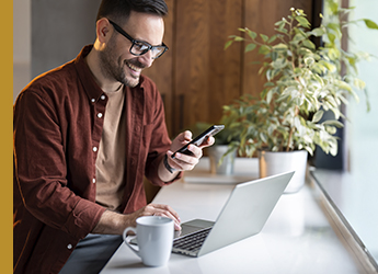 man holding a mobile phone while typing on a laptop